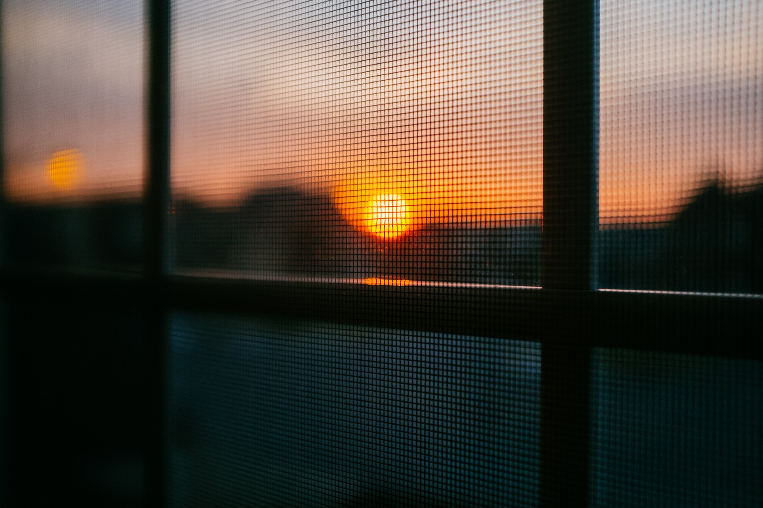 Komarnik na prozoru kroz koji se vidi zalazak sunca